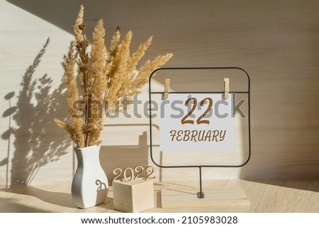 february 22. 22th day of month, calendar date. White vase with dead wood next to the numbers 2022 and stand with an empty sheet of paper on table. Concept of day of year, time planner, winter month. Royalty-Free Stock Photo #2105983028