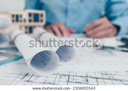 Architect rolls and plans on the table and architect engineer use pen drawing design working on bueprint. House planning design and construction concept.