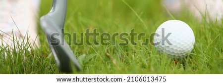Close-up of white golf ball and club. Persons feet on green grass. Macro shot of equipment for game. Competition and tournament. Fresh field for play. Luxury sport concept