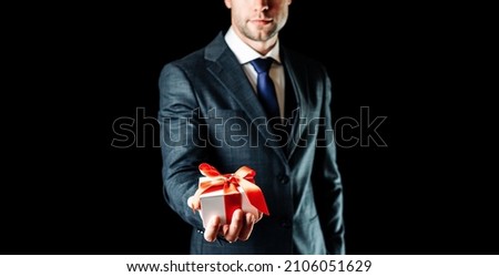 Holding gift box. Happy young business man holding surprise giftbox present with red ribbon isolated on black background. Present for birthday, valentine day, Christmas, New Year