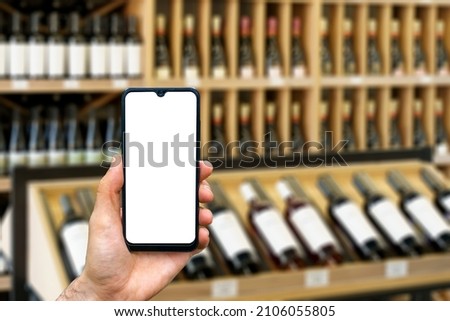 Wine shop with bottles background. Hand with blank smartphone screen one wine backdrop. Buying and ordering alcoholic beverages online