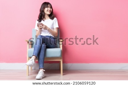 Asian woman sitting on sofa using her phone with a happy expression	 Royalty-Free Stock Photo #2106059120