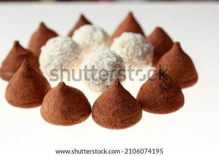 Chocolates made from dark chocolate. White round coconut flakes on the table.