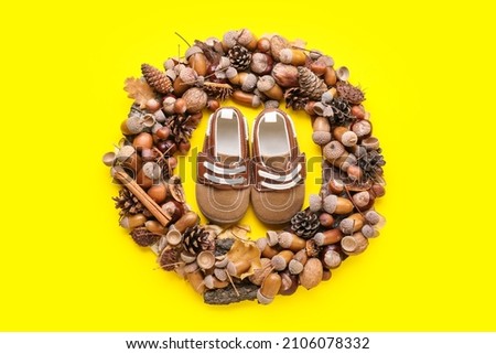 Beautiful autumn wreath and baby shoes on yellow background