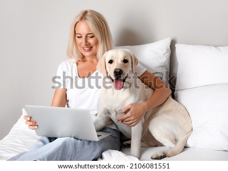Mature woman with laptop and cute Labrador dog on bed Royalty-Free Stock Photo #2106081551