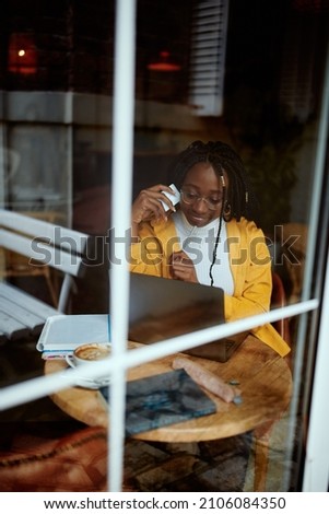 A happy African girl sitting in the coffee shop and using a credit card to purchase online. She is typing card number on laptop keyboard. Picture taken from the outside. E-banking and online shopping.