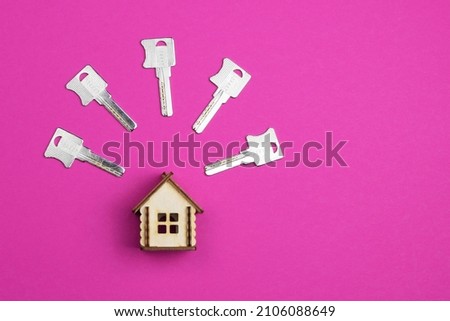 Conceptual composition: a wooden model of a house and a set of house keys on a colored background. Buying, selling, renting real estate. Fashionable colorful photo. Trendy flat lay concept.