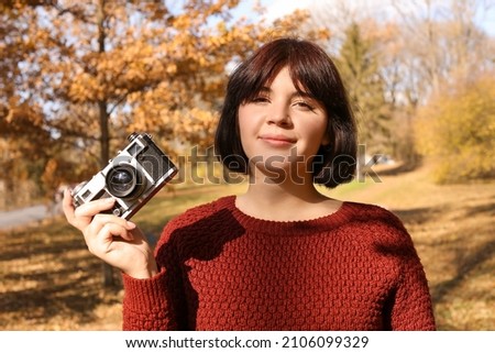 Young woman with photo camera enjoying sunny day in autumn park
