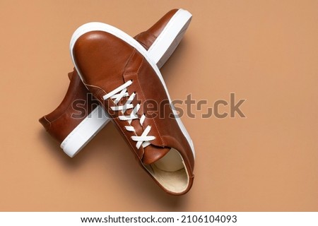 Leather brown men's sneakers with white laces and rubber soles on beige background. Flat lay top view. Men's sports casual shoes. Fashionable sneakers. Male fashion hipster footwear Minimal background Royalty-Free Stock Photo #2106104093