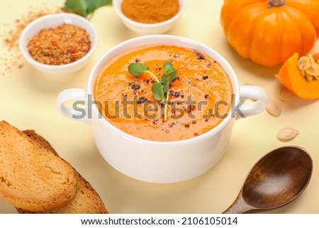 Pot with tasty pumpkin cream soup, spices and toasts on color background, closeup