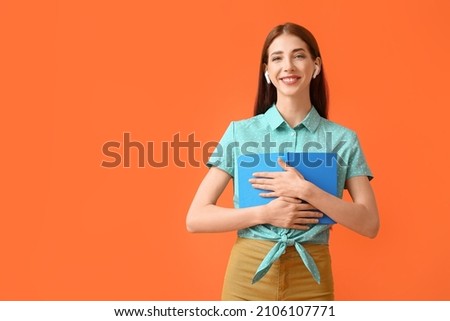 Young woman with earphones and book on color background