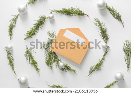 Composition with envelope, card, Christmas balls and coniferous branches on white background