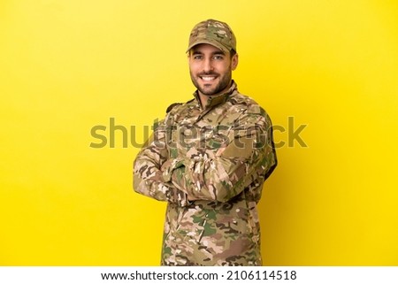 Military man isolated on yellow background with arms crossed and looking forward