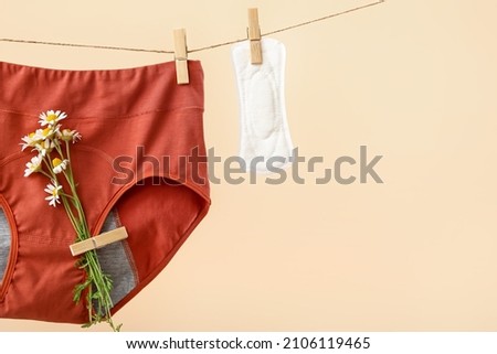 Period panties with chamomile flowers and pad hanging on rope against color background, closeup