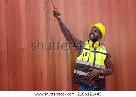 Foreman, a black man in a uniform wearing helmet a safety engineer inspecting a logistics container on time in a container yard.Logistics concept