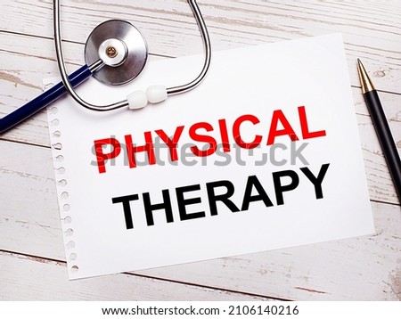On a light wooden table there is a stethoscope, a pen and a sheet of paper with the text PHYSICAL THERAPY. Medical concept