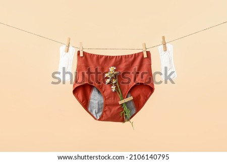 Period panties with chamomile flowers and pads hanging on rope against color background