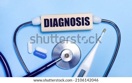On a light gray background, a stethoscope, an electronic thermometer, pills, a wooden block with the text DIAGNOSIS. Medical concept.