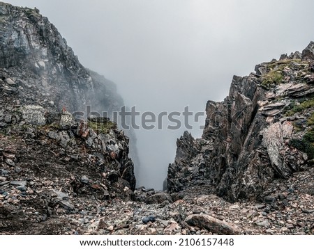 Soft focus. Mountain view from cliff at high altitude. Mystical landscape with beautiful sharp rocks near precipice and couloirs in low clouds. Mountain foggy scenery on abyss edge with sharp stones. Royalty-Free Stock Photo #2106157448