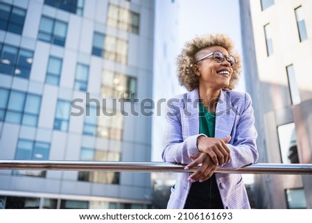 Young African American business woman in trendy outfit and eyeglasses standing on corporate urban district. Inspired creative female professional in the city Royalty-Free Stock Photo #2106161693