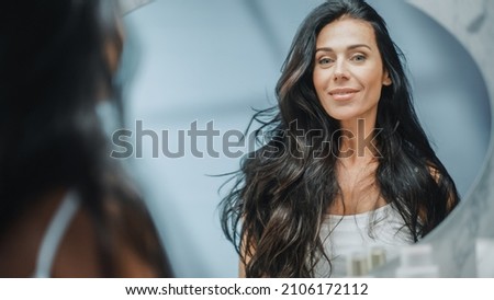 Beautiful Caucasian Middle Aged Woman Looks into Bathroom Mirror, Enjoys Her Looks. Concept for Happiness, Wellbeing, Natural Beauty and Organic Skin Care Products