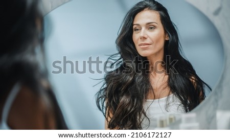Beautiful Caucasian Middle Aged Woman Looks into Bathroom Mirror, Enjoys Her Looks. Concept for Happiness, Wellbeing, Natural Beauty and Organic Skin Care Products Royalty-Free Stock Photo #2106172127