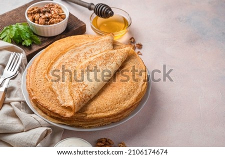 Traditional pancakes with honey, sour cream and nuts on a light pink background. Mardi Gras. Side view.
