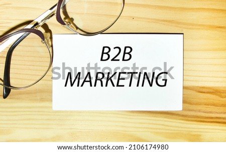 On the business card is the text B2B MARKETING, next to the glasses, the background is a wooden table.