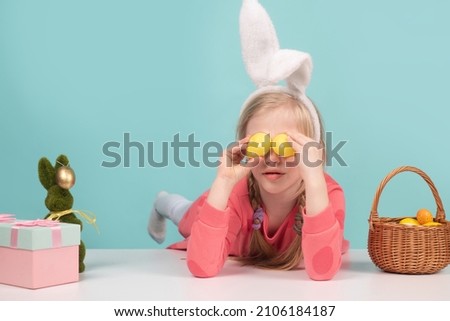 Cute little child wearing bunny ears on Easter day. Girl holding painted eggs on eyes.
