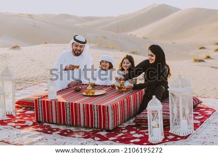 Happy family spending a wonderful day in the desert making a picnic. People from the emirates with traditional clothes making a safari in Dubai Royalty-Free Stock Photo #2106195272