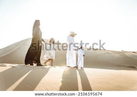 Happy family spending a wonderful day in the desert making a picnic. People from the emirates with traditional clothes making a safari in Dubai Royalty-Free Stock Photo #2106195674