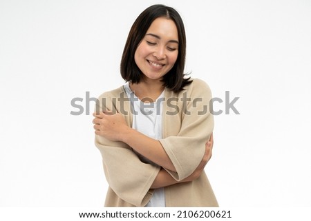 I love myself. Portrait of pleased satisfied asian girl hugging herself and smiling, feeling comfortable and fulfilled, narcissistic egoistic person. Indoor studio shot white background  Royalty-Free Stock Photo #2106200621