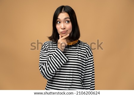 Portrait of thoughtful upset girl pondering serious issues, looking with uncertain hesitant expression, making difficult choice. Indoor studio shot isolated on beige background  Royalty-Free Stock Photo #2106200624