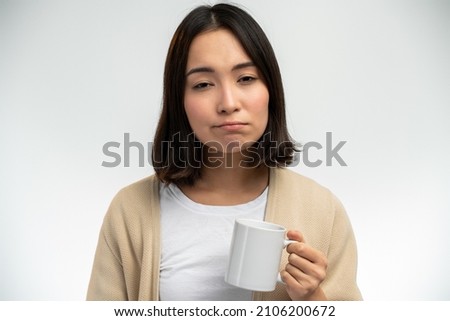 Sleepy asian ethnic female with sleepy eyes holding mug while drinking coffee early in morning against white background 