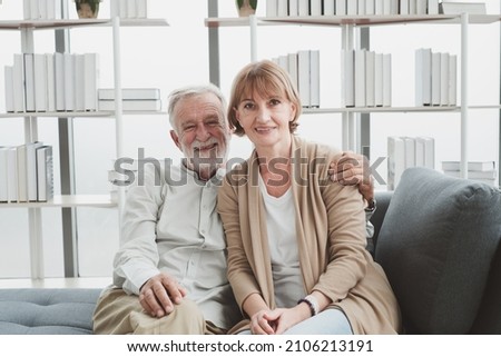 Portrait of senior elderly couple in casual outfit sitting on couch and cuddle together with happy and romantic emotion in living room.