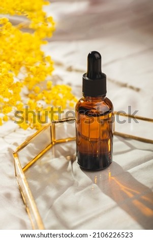 Amber glass bottle with dropper pipette with serum or essential oil on glass plate for product presentation. Skincare cosmetic and dry plants. Beauty concept for face body care