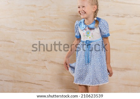 Cute happy laughing little girl giggling as she holds onto the skirt of her pretty blue summer dress, with copyspace