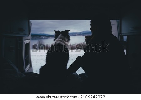 Young woman with dog in the camper van with cup of coffee in her hands. Morning routine with nic view, travel time with dog in winter.