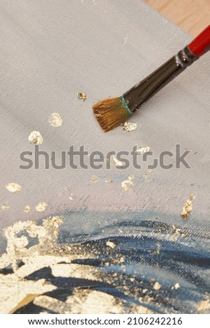 brush on a painting with gray and blue brush strokes and pieces of gold potal