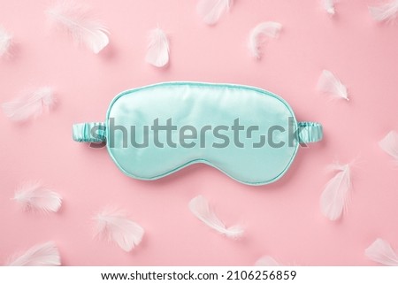 Top view photo of light blue silk sleeping mask and pink feathers on isolated pastel pink background with empty space