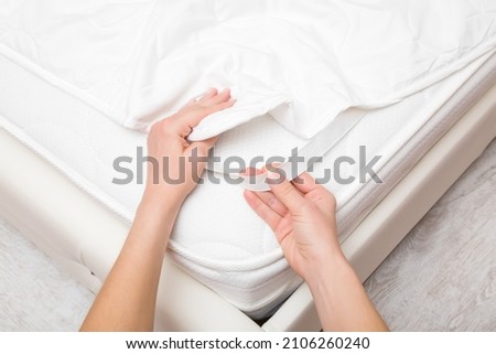 Young adult woman hands putting white cover with elastic band on mattress. Closeup. Point of view shot. Regular bed linen change.  Royalty-Free Stock Photo #2106260240
