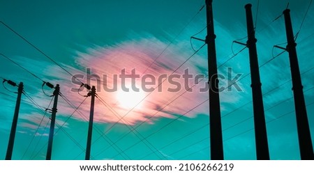 Rising moon in the turquoise-colored sky with pink clouds over the black metal electricity pylons and power lines at night