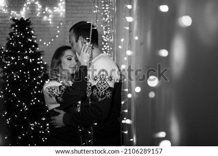 A guy and a girl in identical sweaters celebrate Christmas. A loving couple enjoy each other at the Christmas tree. New Year's love story.
Black and white photo.
