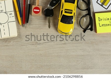 Flat lay composition with driving lessons workbook and toy car on wooden background, space for text. Passing license exam