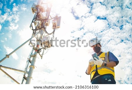 Male engineer uses a smartphone to connect to a 5G network,working in the field near a telecommunication tower that controls cellular electrical installations : Telecom modern communication technology Royalty-Free Stock Photo #2106316100