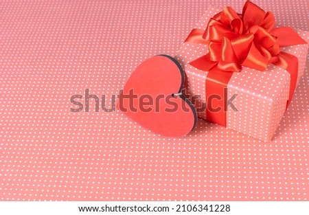 A gift box with a wooden heart on a pink background.