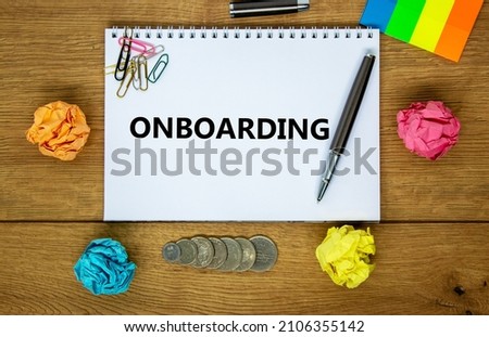 Onboarding symbol. The word 'Onboarding' on white note. Wooden table, colored paper, paper clips, pen, coins. Business, onboarding concept. Copy space.