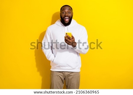 Photo of impressed millennial beard man hold telephone wear white sportscloth isolated on yellow color background