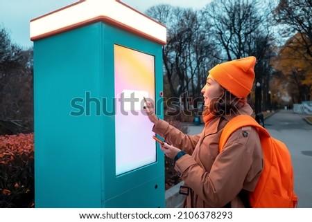 A woman uses a self-service kiosk to print photos from her smartphone on a city street Royalty-Free Stock Photo #2106378293