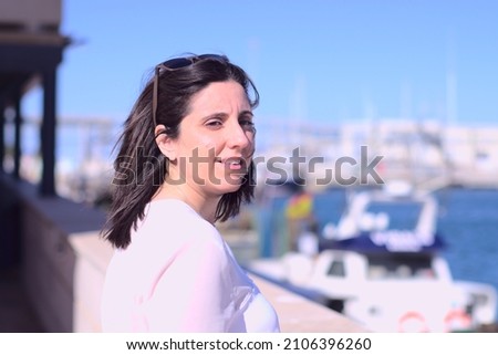 Portrait of caucasian beautiful woman at harbour in sunny day with boats in bokeh background. Happy holiday concept